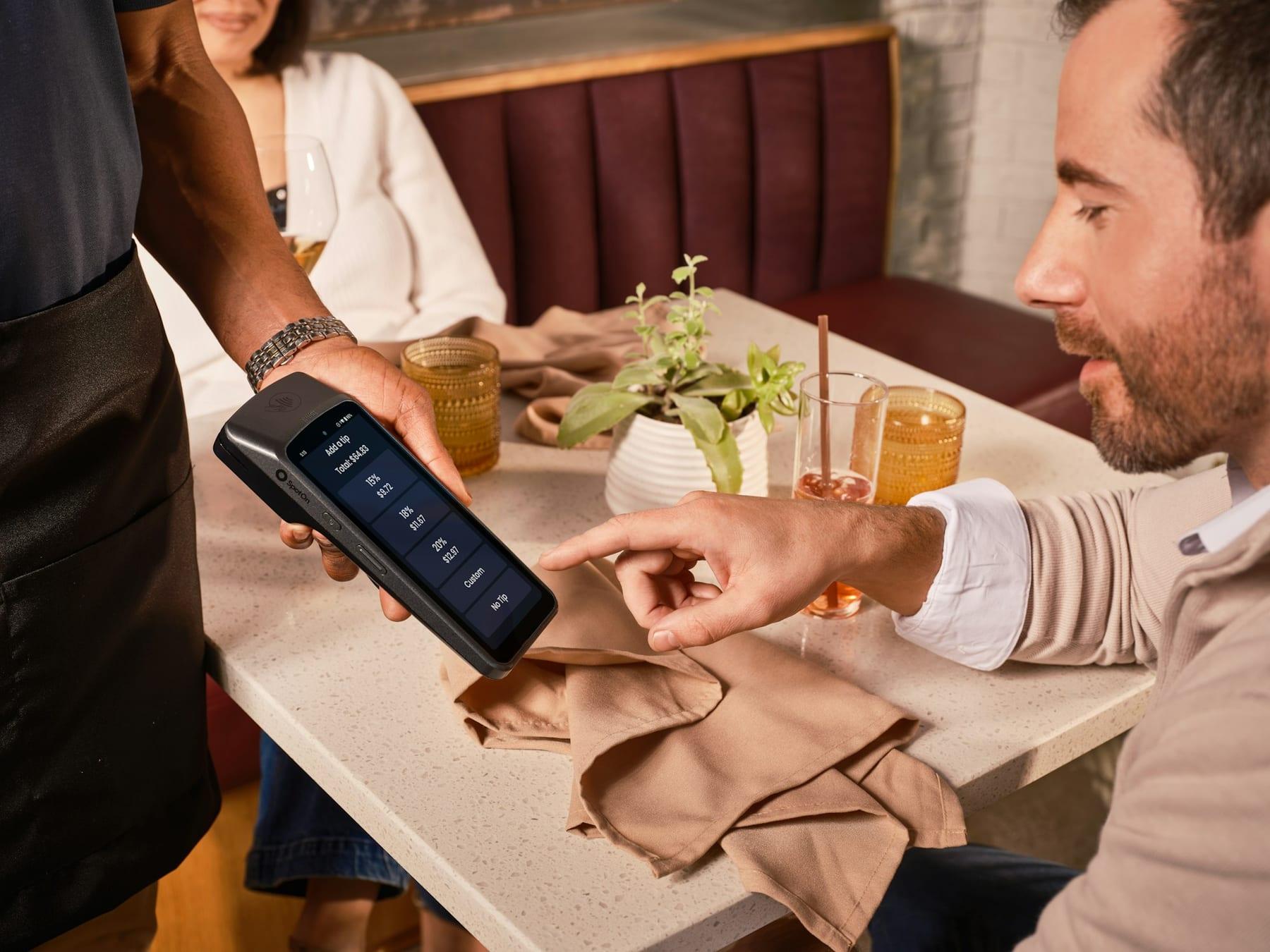 A diner picks a tip on the card terminal held out at his restaurant table