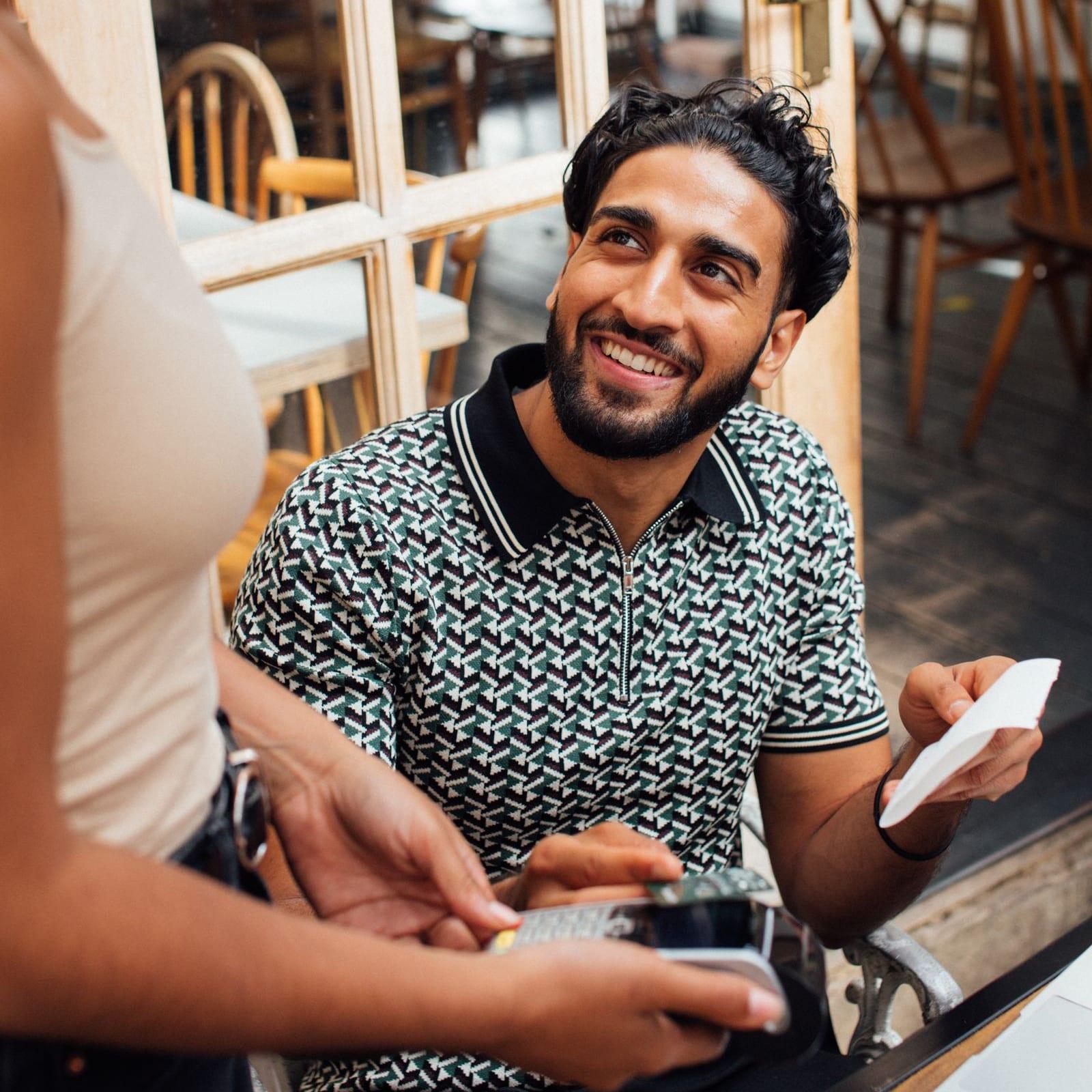 A smiling diner holds the bill at a restaurant table