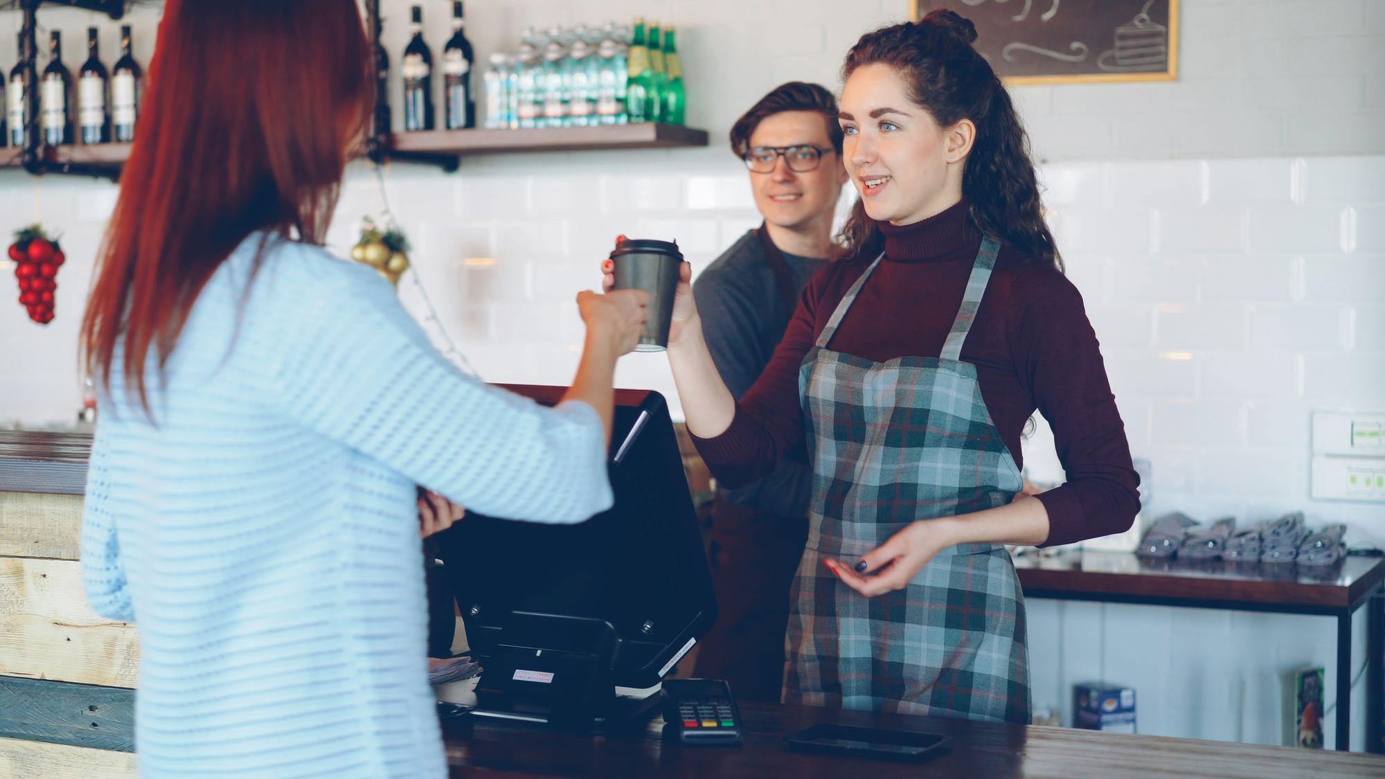 Une barista tend un café à une cliente au comptoir