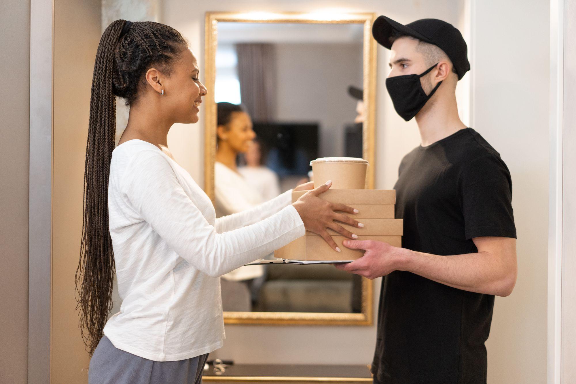 A courier hands a delivery to a smiling customer at the door
