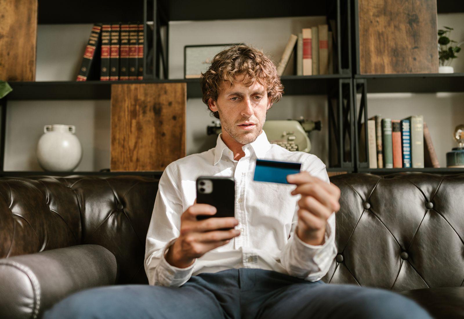 Un homme examine une transaction sur son téléphone, carte à la main