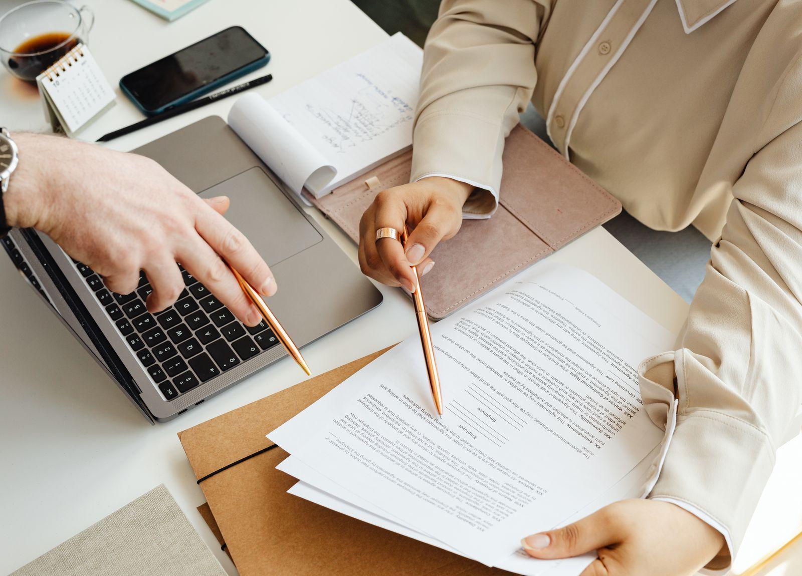 Two people reviewing a printed agreement beside a laptop