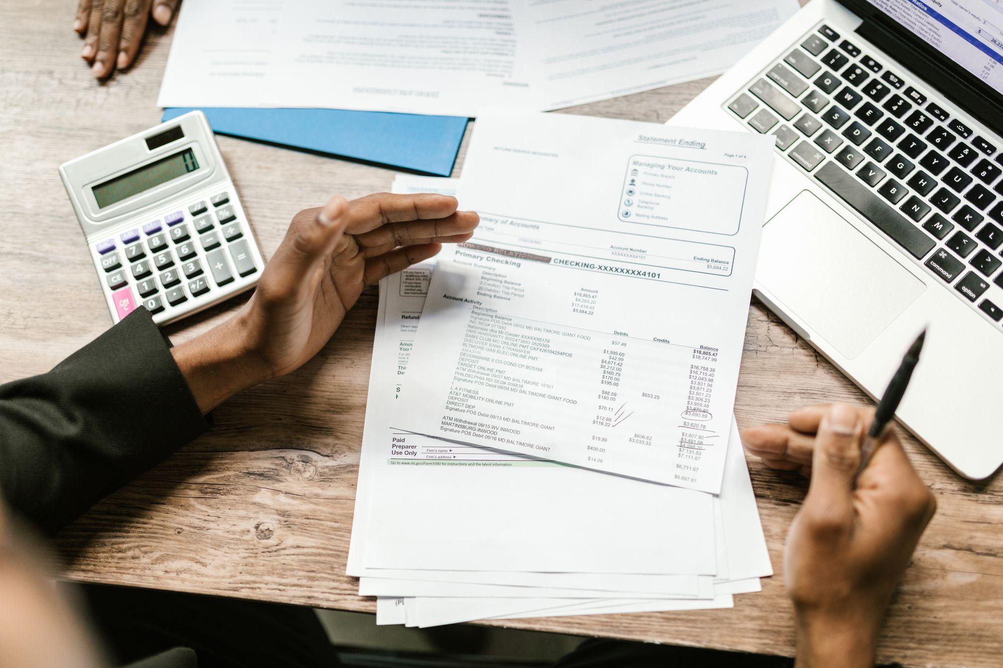 Des mains examinent un relevé de paiement près d'une calculatrice et d'un portable