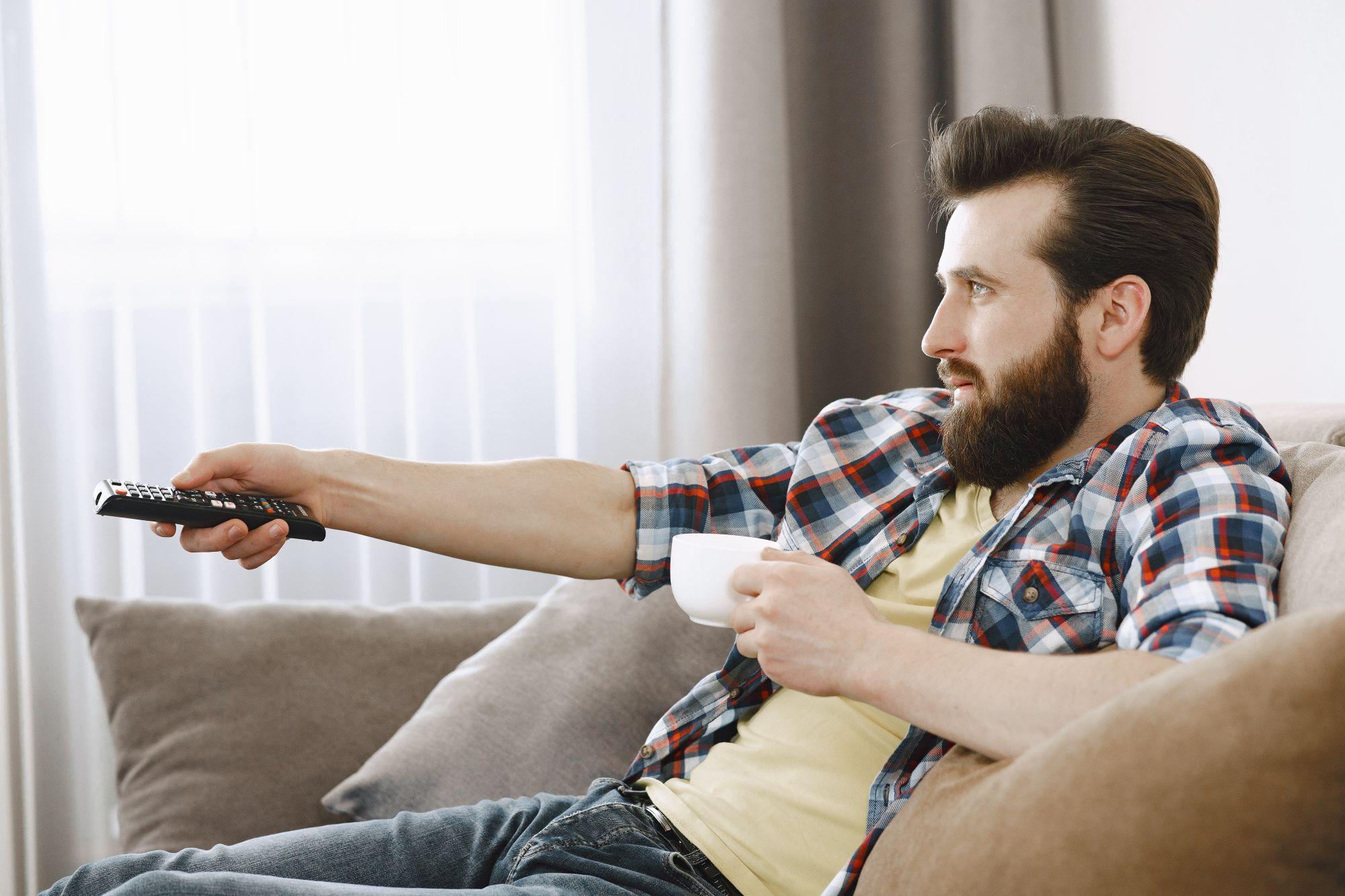 A man relaxes on the sofa with a coffee, remote in hand