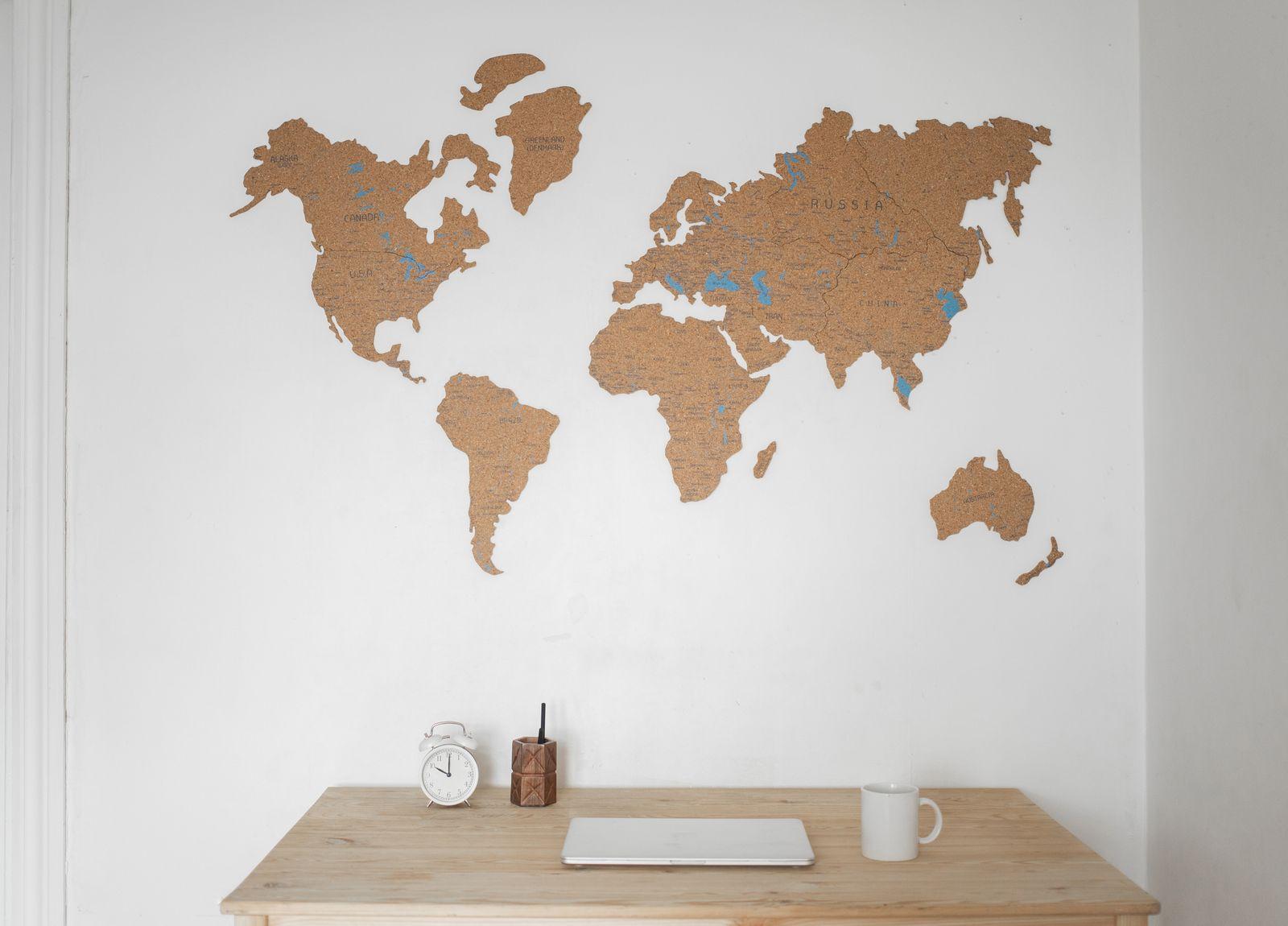 A cork world map on a wall above a desk with a laptop