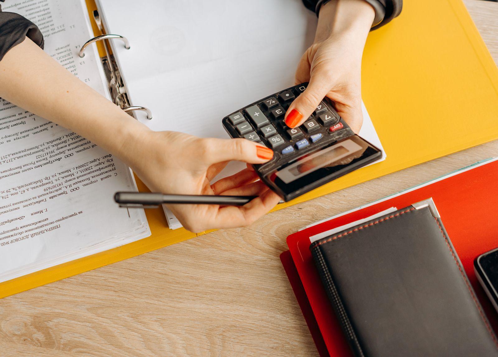 Des mains utilisent une calculatrice au-dessus de factures et d'un classeur