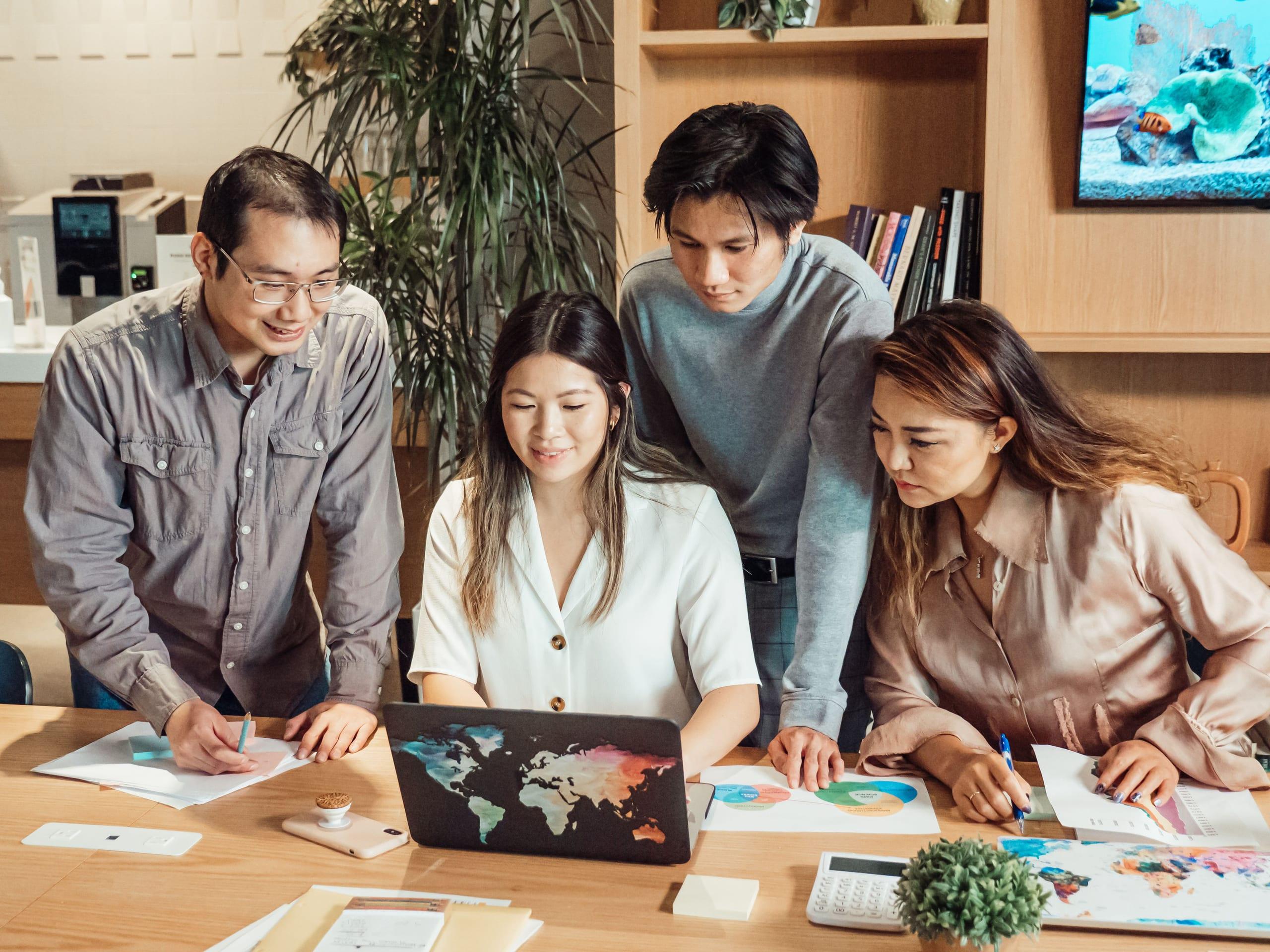 Four colleagues gathered around a laptop in an open office