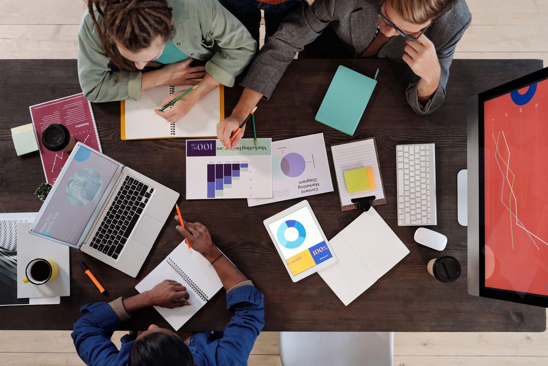 Overhead view of a desk covered in charts, notebooks and laptops