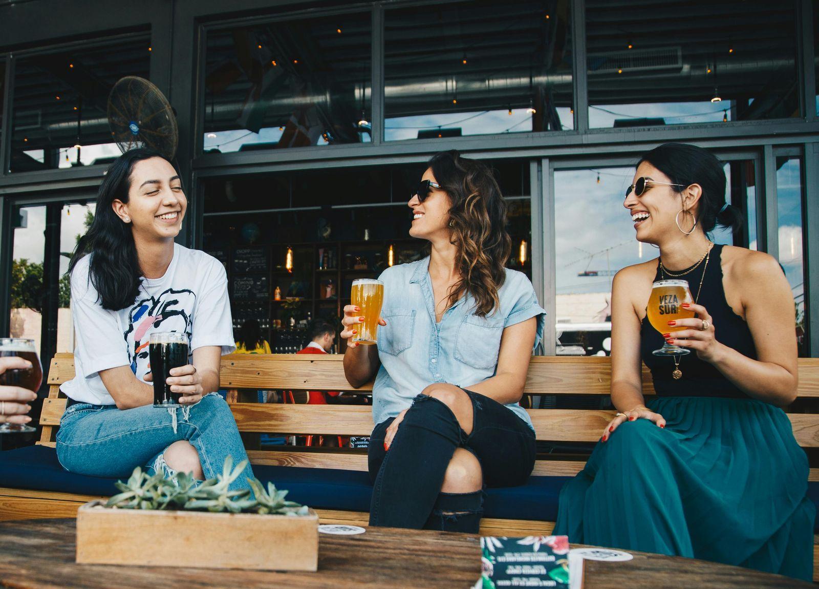 Trois amies qui rient autour d'une bière sur la terrasse d'un bar