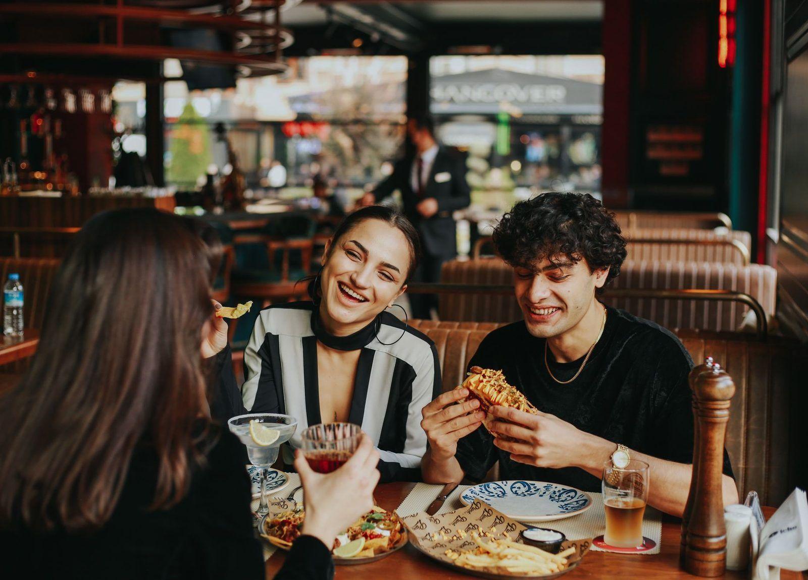 Three friends laughing over dinner and drinks at a restaurant table