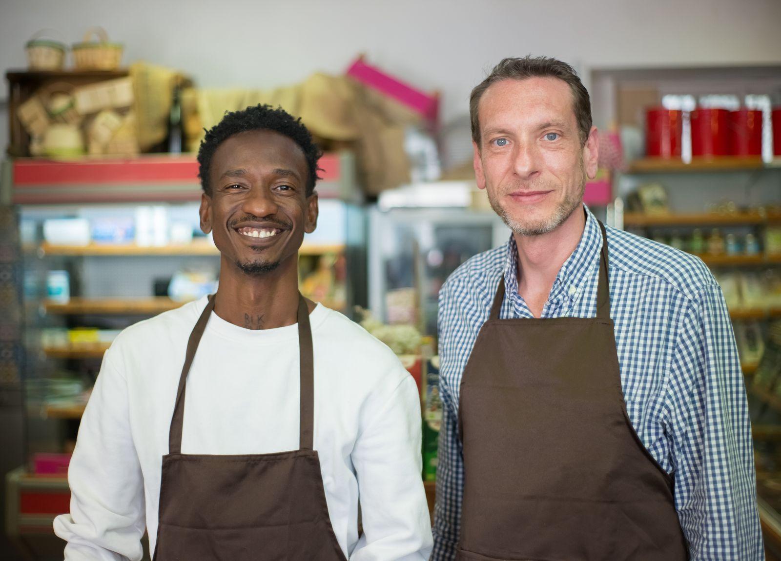 Two shop owners in aprons behind their counter